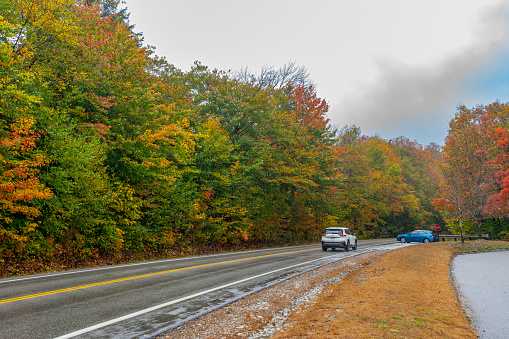 Kancamagus Highway, New Hampshire, USA - October 2023. Autumnal leaf coloured forests on the Kancamagus Highway towards White Mountain with SUVs on a wet road.