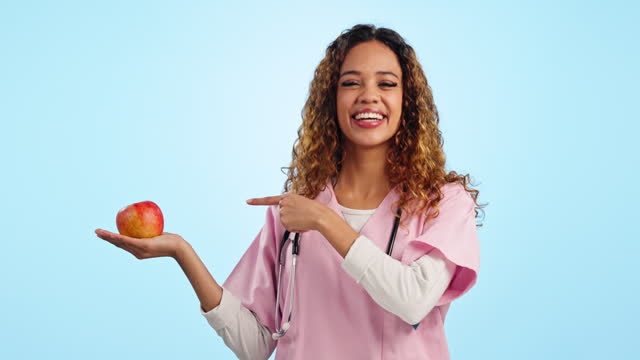 Studio, happy woman or face of doctor and apple in hand for diet advice, healthcare or healthy food. Smile, portrait and nurse with review, feedback or medical guide in nutrition on blue background.