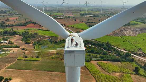 cuacasian man and woman electric engineer discussing for maintenance wind turbine or windmill on the top of wind turbine.Sustainable,renewable,clean energy concept.aerial  top view.