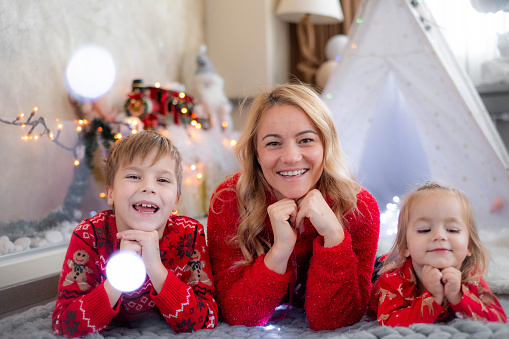 Mom and her children are dressed in Christmas sweaters and take pictures next to the Christmas tree and decorations