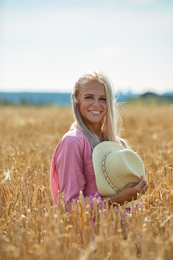 Woman with long blond hair and a straw hat in a wheat field