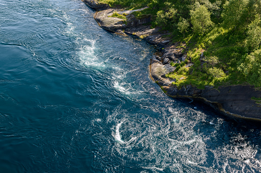 Aerial view of Saltstraumen's fierce tidal currents carving through the water, creating mesmerizing whirlpools by Norway's rocky shores
