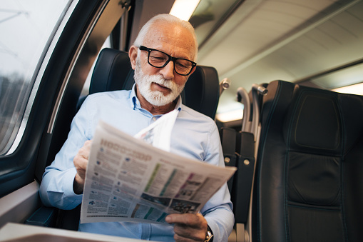 An elderly businessman travels by train and reads a newspaper