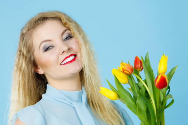 International women day, eight march. Beautiful portrait of pretty woman blonde hair with red yellow tulips, fashion make up, elegant dress. Mother day. On blue