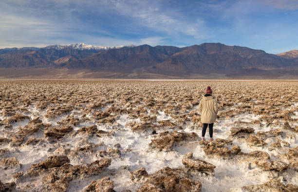Embarking on a formidable journey, intrepid female hiker navigate the unforgiving terrain of Devil's Golf Course in Death Valley National Park. The arduous trek through rugged salt and mineral deposits adds a unique challenge