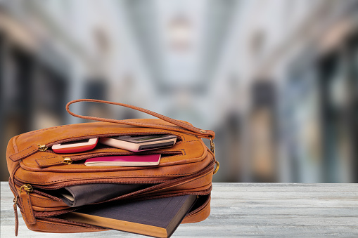 Business and travelling concept. A brown luxury leather wrist handbag with businessman accessories on the table above blurred office space. Opened wallet.