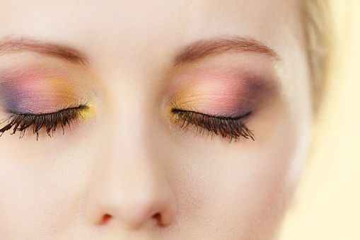 Woman having beautiful colorful eye makeup in purple yellow and pink shades, eyes closed.