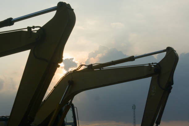 Excavator on road construction. Screeding gravel for installing borders, curbs concrete blocks at road. Roadworks on sunset. Bucket excavator on road construction at construction site.