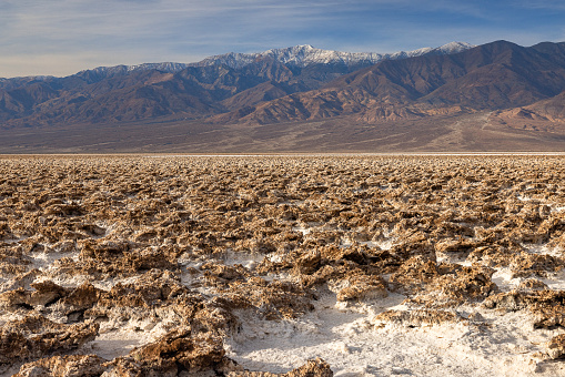Salt flats in Badwater Basin in Death Valley national park , California during sunset with majestic mountains.