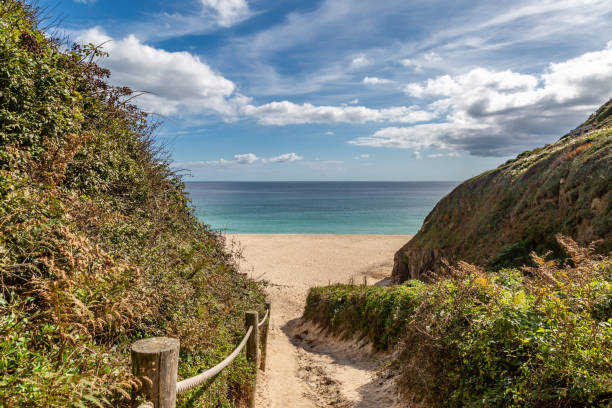 Looking along a pathway leading to the sandy beach at Porthcurno on the Cornish coast A view down a footpath to Porthcurno beach, with a blue sky overhead cornwall england stock pictures, royalty-free photos & images