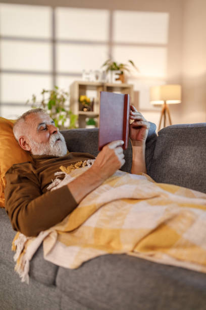 istock Happy mature man lying on the sofa and reading a book 1960329084