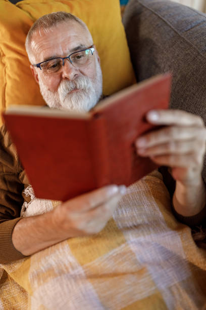istock Happy mature man lying on the sofa and reading a book 1960329086
