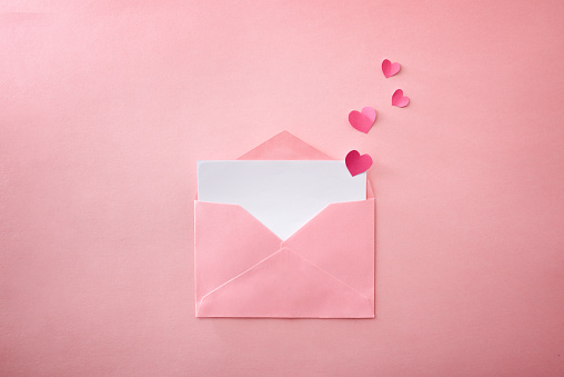 Open pink envelope with empty white sheet with heart cutouts coming out on pink textured background. Top view.