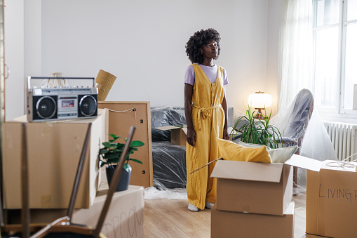 A young African-American woman gazes wistfully at the room of her soon-to-be former home. With each packed box, a piece of nostalgia surfaces, and a sense of melancholy hangs in the air.