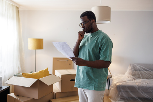 Photo of an African-American standing in his new home and confusedly reading a buyer contract