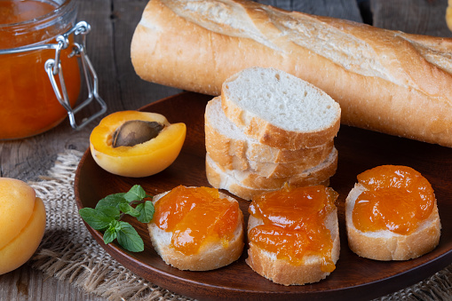 Toasts of bread with apricot jam and fresh fruits with mint on wooden table. Tasty breakfast.