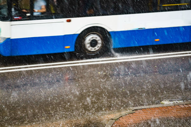 Rain in city. Bus driving on street during downpour. Water splashes, spills on roadway. Autumn season