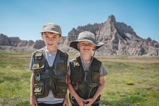 Two brothers wearing junior ranger vests in front of rock formations in Badlands National Park.