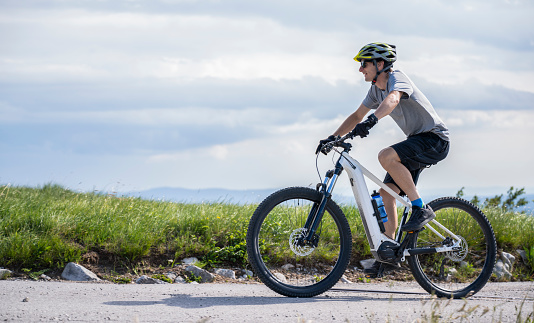 Male sportler riding electric mountain bike on green meadows landscape. Healthy lifestyle concept.
