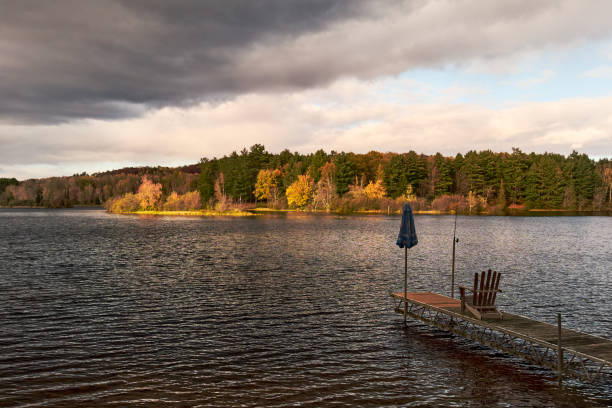 A view of the sunset from a small dock on the lake with an outdoor empty chair and a blue shade in a stormy day