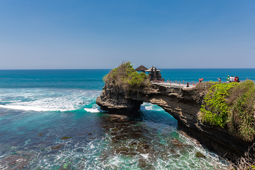 The natural rock arch on a sunny day at Pura Batu Bolong near Tanah Lot Temple in Bali, Indonesia.