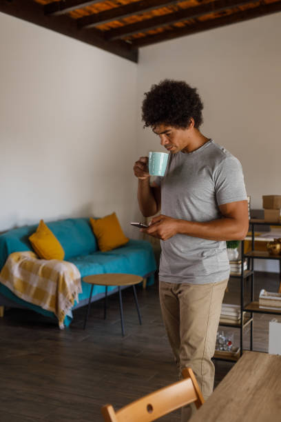Man walking through his home, using smart phone and enjoying coffee