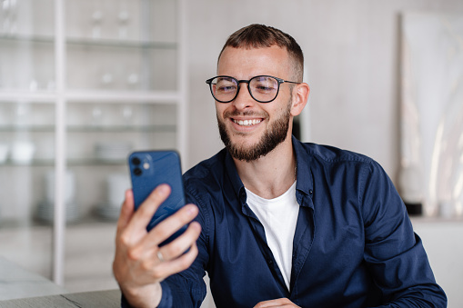 Happy young man with glasses using a smartphone, in a modern interior setting