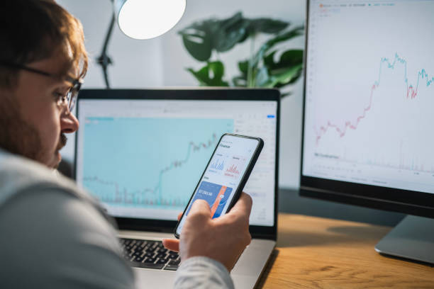 istock Man looking at currency trading app on his smart phone from his home office. 1960426989