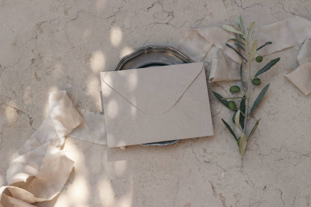 istock Mediterranean wedding stationery. Craft envelope, vintage silver plate. Dappled light. Olive tree branches, fruit. Beige marble background, floor. Summer holiday design. Birthday mock-up. Flatlay, top 1960430246