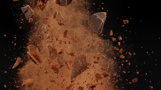 Super slow motion shattered bits and pieces of dark bitter chocolate and cocoa powder tossed in the air cut out on black background