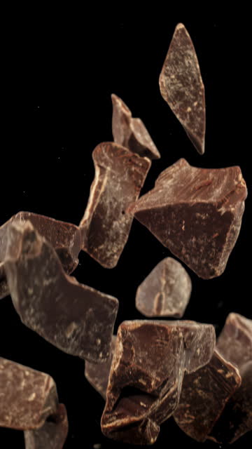 Super slow motion shattered bits and pieces of dark bitter chocolate tossed in the air cut out on black background