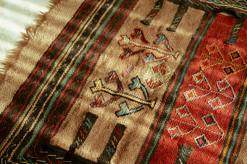 A close-up photo of a pattern and design on an Iranian rug with sunlight shining on it.