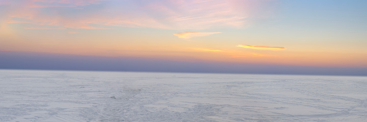 Panoramic view: Winter sunset over frozen sea covered with snow