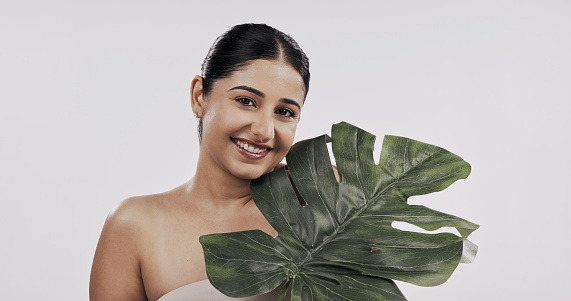 Skincare, plant and portrait of happy woman in studio with natural, beauty or cosmetics on white background. Palm leaf, face and female model with monstera for wellness, cleaning or organic benefits