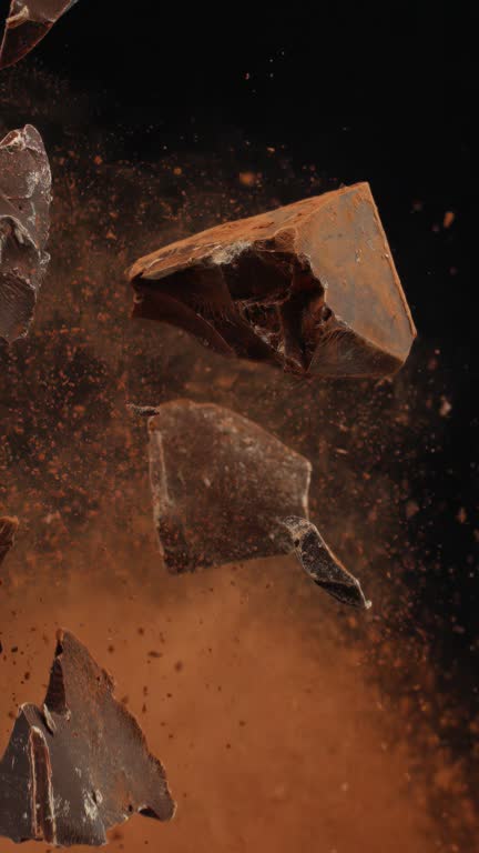 Super slow motion shattered bits and pieces of milk chocolate and cocoa powder tossed in the air cut out on black background