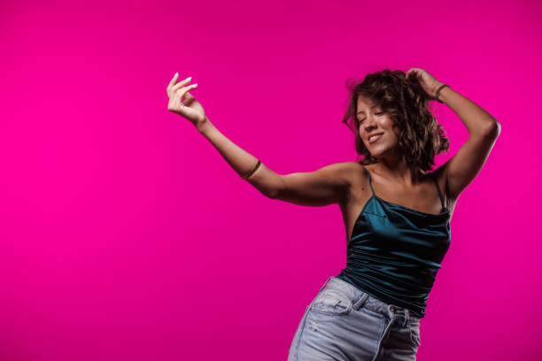 Portrait of joyful young brunette having fun and dancing freely against bright pink background.