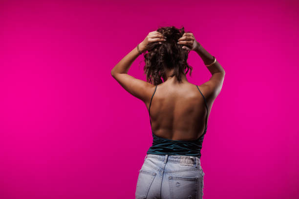 Front view of cool young brunette having fun posing and dancing against bright pink background.