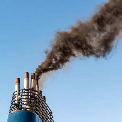 Thick smoke polluting a clear blue sky, as a large industrial ship's engines create exhaust fumes.