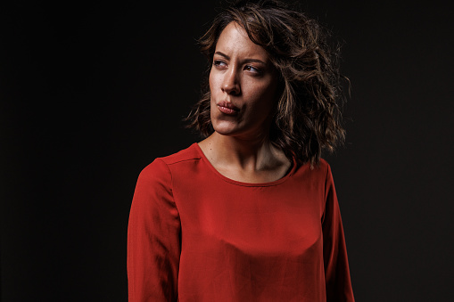 Portrait of unsure young woman, standing against black background, looking away, confused, contemplating.