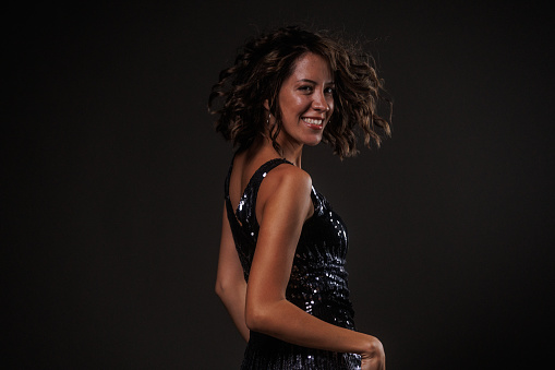 Candid shot of cool young woman, in a sparkly little black dress, having fun and enjoying dancing against dark gray background.