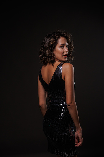 Candid shot of cool young woman, in a sparkly little black dress, having fun and enjoying dancing against dark gray background.