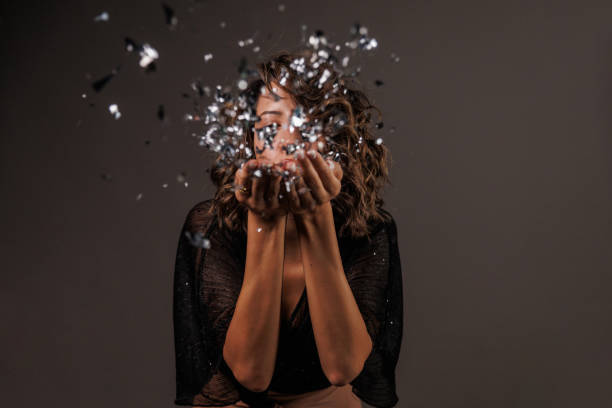 istock Cute brunette blowing a handful of silver colored confetti 1960508273