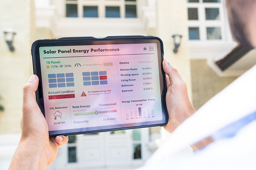 Close-up of a hand holding a digital tablet, revealing the solar panel energy performance status on the display at his home.