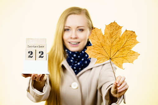 Woman holding calendar with first autumn day 22 september and big leaf. Studio shot on yellow background.