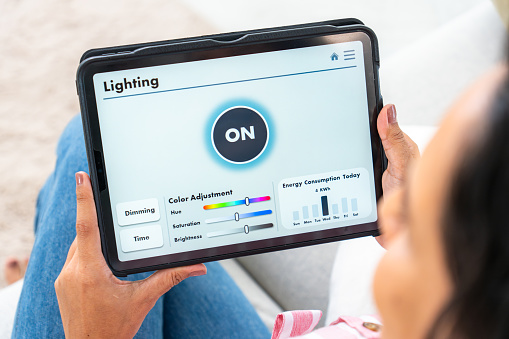 Close-up of lighting screen on the mobile app, a beautiful mid-adult woman using voice commands to switch on the light, control the brightness, and set a comfortable temperature in his house on the mobile app on her tablet, home automation