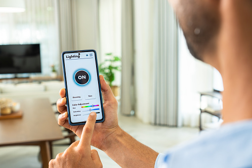 A Latin mid-adult businessman using voice commands to switch on the light, control the brightness, and set a comfortable temperature in his house by using the mobile app on his smartphone, a smart home concept
