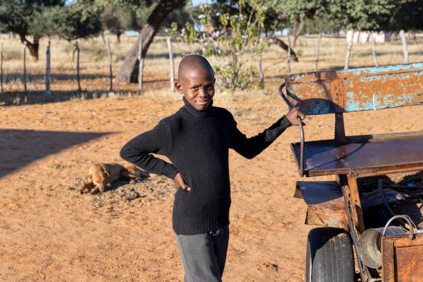 young village african child with bald head standing outdoors next to a donkey cart