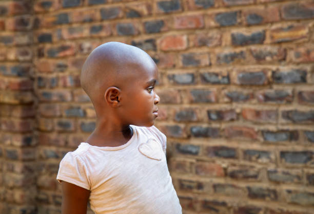 young village african with bald head standing outdoors in front of a brick wall