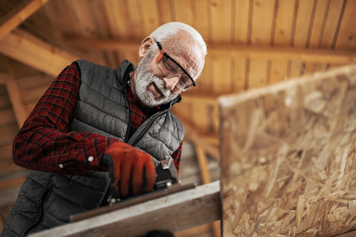 Senior male craftsman at his workshop sawing wood