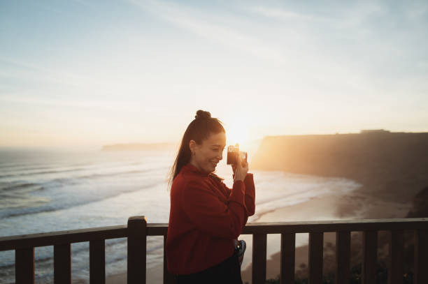 A young woman taking a picture with a camera at sunset